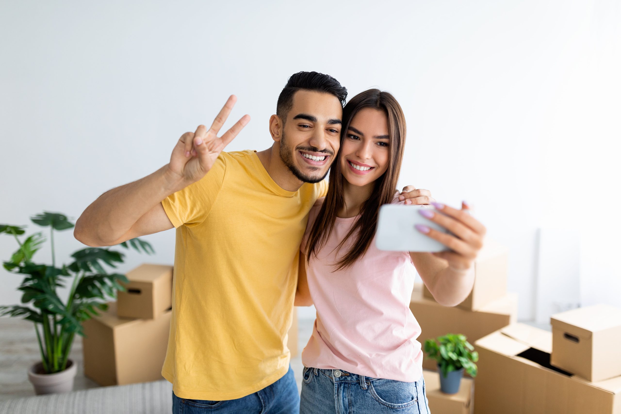 Smiling young couple taking a selfie of them moving into their new home with boxes in the background